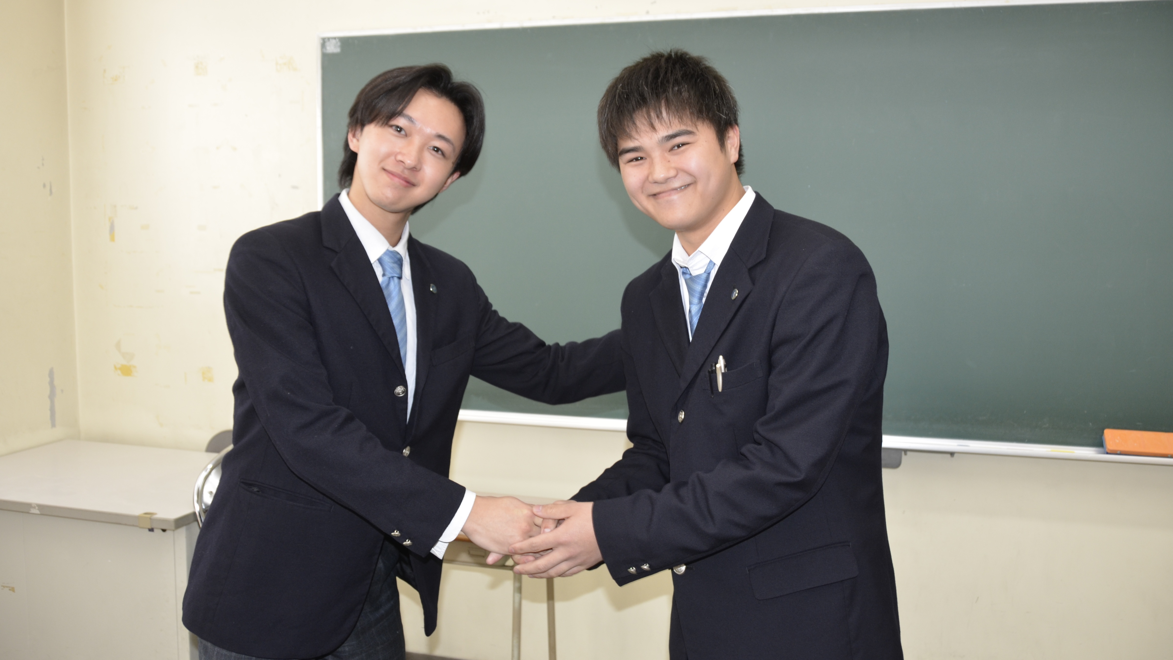 クラーク記念国際高等学校 久留米キャンパスの生徒会引継ぎ式。笑顔で握手を交わす新旧会長と、真剣に助言を聞く生徒会メンバー。